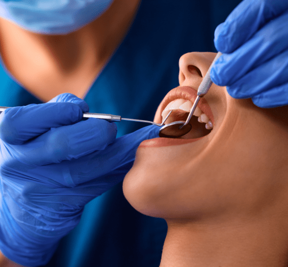 A dentist in a blue mask and gloves examines a patient's open mouth using dental tools, conveying a clinical, professional setting.