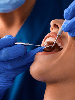 A dentist in blue gloves examines a patient's open mouth using dental tools. The patient appears calm, and the setting is clinical and professional.
