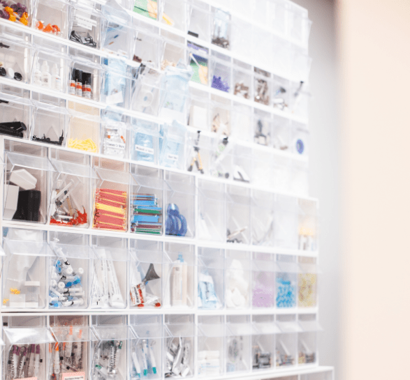 Transparent storage bins filled with various medical supplies line a wall. The bins contain tubes, syringes, and other items, organized neatly by type.